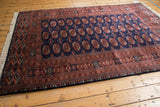 High-angle view of a vintage Bokhara carpet with a lustrous navy field and rust-colored gul design.