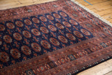 Corner of a vintage Bokhara rug with a plush navy pile, rust-colored gul medallions, and short ivory fringe.
