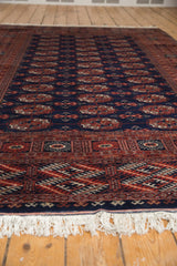 Low angle view of a vintage Bokhara carpet's geometric border, white fringe, and lustrous navy pile.
