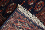 Folded corner of a Pakistani Bokhara rug showing the tight weave, intact selvage, and ivory fringe.