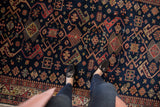 Navy blue vintage Romanian Kuba carpet, geometric patterns, colorful border, and visible feet.