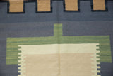 Abstract Kilim rug detail showing interlocked geometric border in charcoal, green, and neutral tones.
