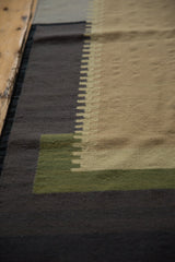 Architectural stepped geometric pattern in charcoal, beige, and green flatweave.