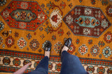 Vintage rug with ochre field, playful floral motifs, and pawn design border.