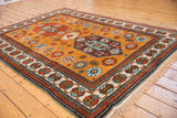 Vintage Kazak rug featuring brown and aqua medallion, ochre floral field, and vine border.