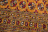 Close-up of the vintage Bokhara's intricate border and repeating red and charcoal gul medallions.