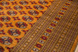 Detailed view of the plush wool pile, gul medallions, and geometric border of a tangerine Bokhara carpet.