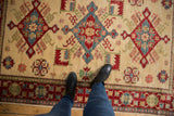 Hand-knotted Pakistani Kazak rug featuring vibrant ivory, red, blue geometric motifs underfoot.