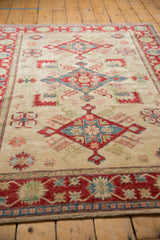 Pakistani Kazak design rug displaying a cherry red floral border and ivory field with serrated motifs.
