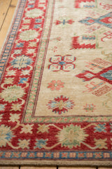Cherry red border and ivory field with detailed geometric floral motifs on a Pakistani Kazak rug.