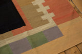 Detail of a contemporary Kilim rug corner, with abstract blocks in black, orange, green, and tan.