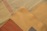 Folded contemporary Kilim carpet shows abstract beige, tan, and faded rust patterns.