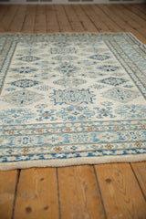 Low angle view across the plush, full pile of a Kazak rug with ivory, blue, and sand geometric motifs.