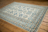 Stepped geometric medallions in blue and sand repeat across the ivory field of a Pakistani Kazak rug.