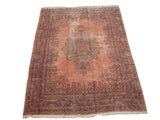 Angled view of a vintage Persian Kerman carpet with its ornate starburst medallion on a rose field.