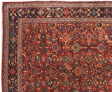 The intricate navy blue border and dense brick-red floral field of a vintage Mahal carpet.