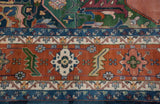 Geometric borders of a vintage Indian Serapi carpet in madder root, denim blue, and forest green.
