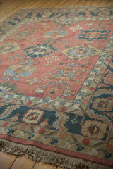Dusty blush floral field meeting a dark navy serrated border; vintage Indian Serapi rug fringe.
