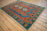 Rug corner with gem-tone terra cotta, sapphire blue, emerald green geometric patterns, and fringe.