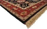 Corner of Serapi Soumac rug, wine red border with floral vines, black field, beige fringe.