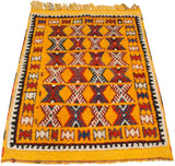 Angled view of a plush Moroccan Murat rug with saffron yellow pile and geometric hourglass patterns.