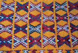A close view of the full pile showing geometric hourglass plant motifs in saffron, blue, and red.