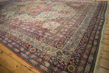 Intricate navy and red floral borders frame the sprawling ivory field of an antique Kermanshah carpet.