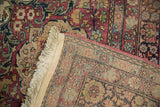Corner view of an antique Kermanshah carpet revealing the hand-knotted back and faux fringe.