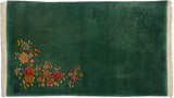 Upper corner of the emerald green Art Deco rug, featuring embossed floral spray and ivory fringe.