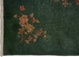 Nichols Art Deco rug corner: dark green ground with carved floral sprays in rust and beige, natural fringe.