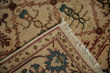 Folded vintage Agra rug corner displaying ivory pattern, wine red border, and secured fringe.