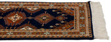Turkmen runner detail: navy field, rust geometric medallions, hook motifs, ivory fringe.