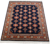 Corner of Indian Turkmen rug with rust geometric border and navy field's germinating plant motifs.