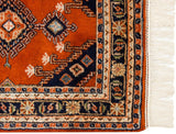 Intricate corner of vintage Turkmen rug showing rust, navy, and ivory geometric border motifs with fringe.