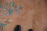 Pale dusty apricot rug pile with ornate celadon, blush, and coffee floral motifs.