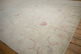 Angled view of an ivory Kerman design carpet with staggered rows of pale raspberry floral bouquets.