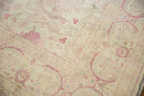 Corner detail of a distressed Kerman design rug with ivory and pale raspberry florals.