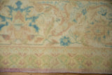 Evenly worn, low pile of a distressed carpet with pale blue and dusty rose motifs.