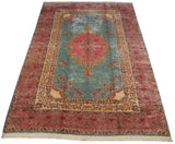 Vintage Kerman carpet from an angle, featuring a pink scalloped medallion on a powder blue field.