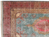 Corner of a vintage Kerman carpet with pink millefleur borders, a blue field, and a scalloped medallion.