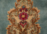 Close-up of a Rococo-stylized floral motif in pink, blue, and gold on a plush Kerman carpet.