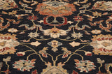 Angled view of floral and cloudband motifs on the plush charcoal black pile of a new Agra carpet.