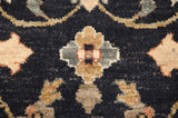 Close-up of a floral palmette in sand, copper, and slate blue on the plush charcoal black pile of an Agra carpet.
