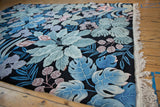 Dimensional jungle motif in blue, green, blush on black vintage carpet, showing fringe.