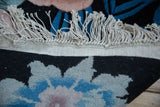 Vintage Jungle carpet's intact beige fringe, secured edge, and blue, black floral pile.