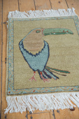 Pictorial Armenian toucan rug's blue body, blush feet, colorful tail feathers, and fringe.
