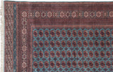 The intricate, multi-banded geometric border and ivory fringe of a vintage Bokhara carpet corner.