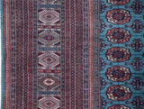 Close-up of a vintage Bokhara carpet showing its intricate red border and powder blue field with gul medallions.