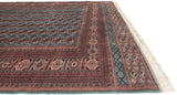 Angled view of the intricate geometric borders and neat ivory fringe on a vintage Bokhara carpet.