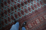 Angled view of the fine Bokhara carpet's plush pile, featuring repeating red and navy gul medallions.